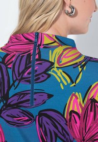 T-shirt z krótkim rękawem w niebieskim kolorze, zdobiony odważnymi wzorami kwiatowymi w różowym, fioletowym i żółtym. Zawiera zamek błyskawiczny z tyłu.