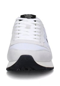 Scarpe sportive bianche con parte superiore in pelle e suede, punta rotonda e suola piatta in gomma nera. Presentano una linguetta nera con testo bianco.