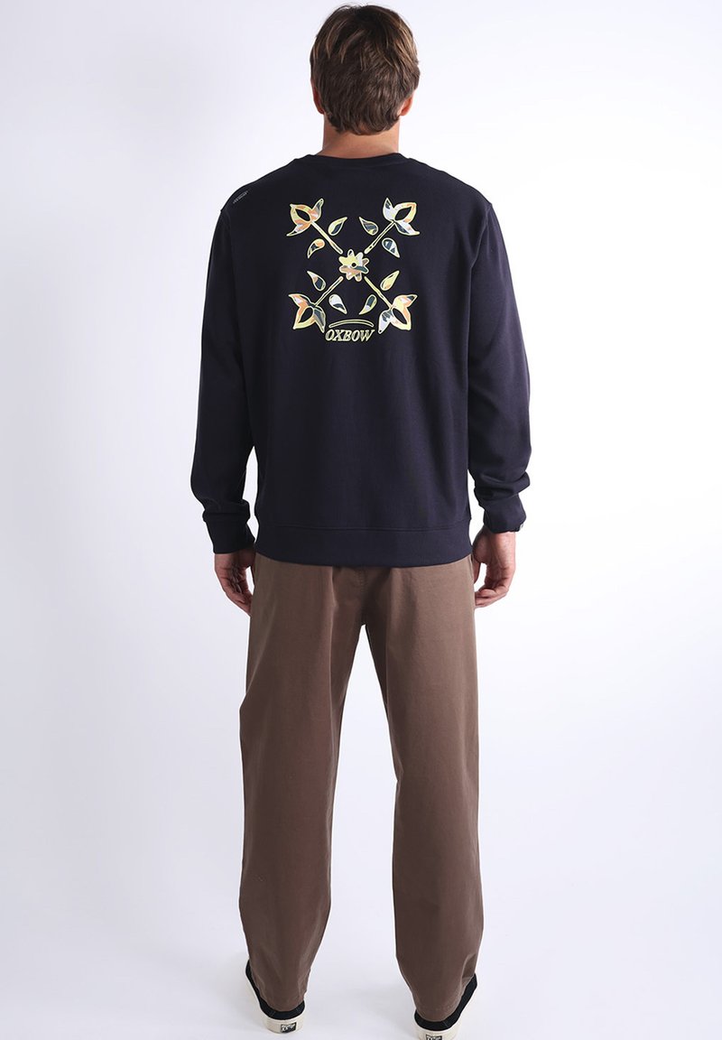 Sweatshirt marine avec un graphique floral dans des couleurs claires au dos, associé à un pantalon beige. Matériau en coton, avec des poignets et un ourlet côtelés.