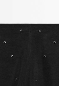 Tissu noir avec huit œillets métalliques espacés uniformément, disposés en un motif irrégulier sur fond blanc.