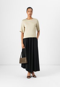 Beige kortermet topp, svart plissert maxiskjørt, holder en brun teksturert håndveske. Svart høye hæler fullfører antrekket. Enkel, elegant design.