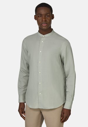 Chemise à manches longues vert clair avec un col montant, fermeture à boutons et ourlet légèrement courbé. Tissu doux et lisse avec une texture subtile.