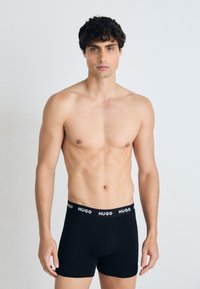 Schwarze Boxer-Shorts aus Baumwolle mit einem weichen elastischen Bund, der den Markennamen "HUGO" in Weiß trägt. Glatte Textur, körpernahe Passform.