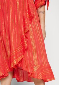 Rotes Kleid mit goldenen metallischen Streifen, ausgestattet mit Rüschensaum entlang dem Saum und den Ärmeln. Leichter Stoff mit fließendem Design.