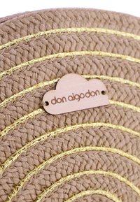 Tapete redondo tejido en un beige natural con tres hilos metálicos dorados y una etiqueta de madera en forma de nube etiquetada "don algodon".