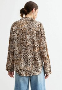 Camicia a maniche lunghe con stampa leopardata in tessuto morbido e testurizzato; presenta un colletto, chiusura con bottoni sul retro e una vestibilità comoda con maniche ampie.