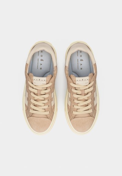 Ζεύγος μπεζ σουέντ αθλητικών παπουτσιών με κρέμ κορδόνια και σόλες, με την επωνυμία "Hogan" στο εσωτερικό και στη γλώσσα, εμφανιζόμενα από ψηλά σε λευκό φόντο.