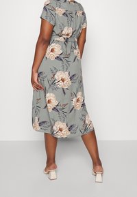 Kukkamekko midimittaisena, lyhyillä hihoilla, vaaleanvihreällä taustalla, suurilla beigellä pionikuvioilla, vyötäröltä kireä ja sileä kangas. Neliöpohjaiset kengät.