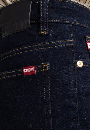 Dunkelblaue Jeans aus Denim mit kontrastierendem goldenen Nähten, Lederetikett am Bund und kleinen roten "BIG STAR"-Tags an den hinteren Taschen.
