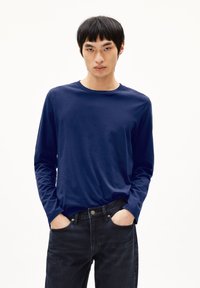 Navyblaues Langarm-T-Shirt aus weichem Baumwollstoff, mit rundem Halsausschnitt und legerem Schnitt. Kombiniert mit dunklen Jeans.