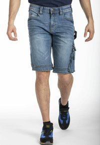 Shorts cargo en denim bleu clair, présentant une coupe régulière, plusieurs poches et des coutures contrastées, assortis à des baskets noires et bleues.