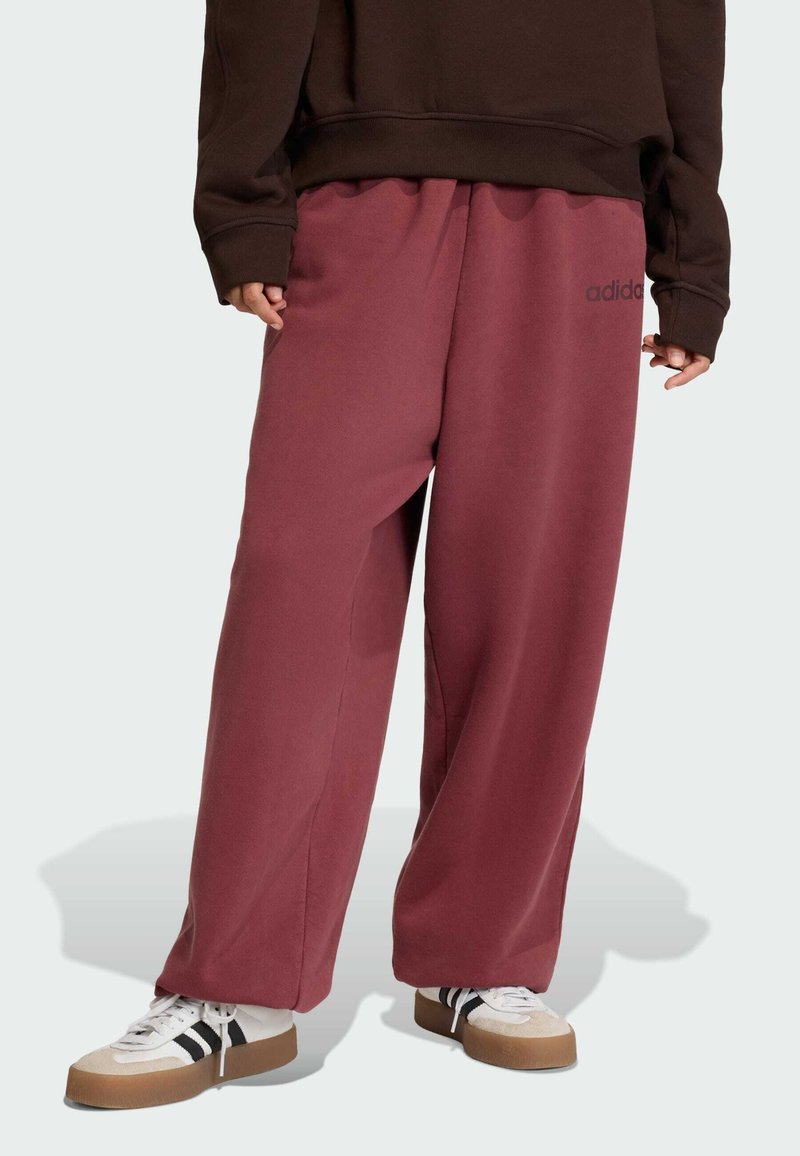 Pantalones de chándal anchos color burdeos hechos de una tela suave, con una cinturilla elástica y un pequeño logo negro de adidas en el lateral.