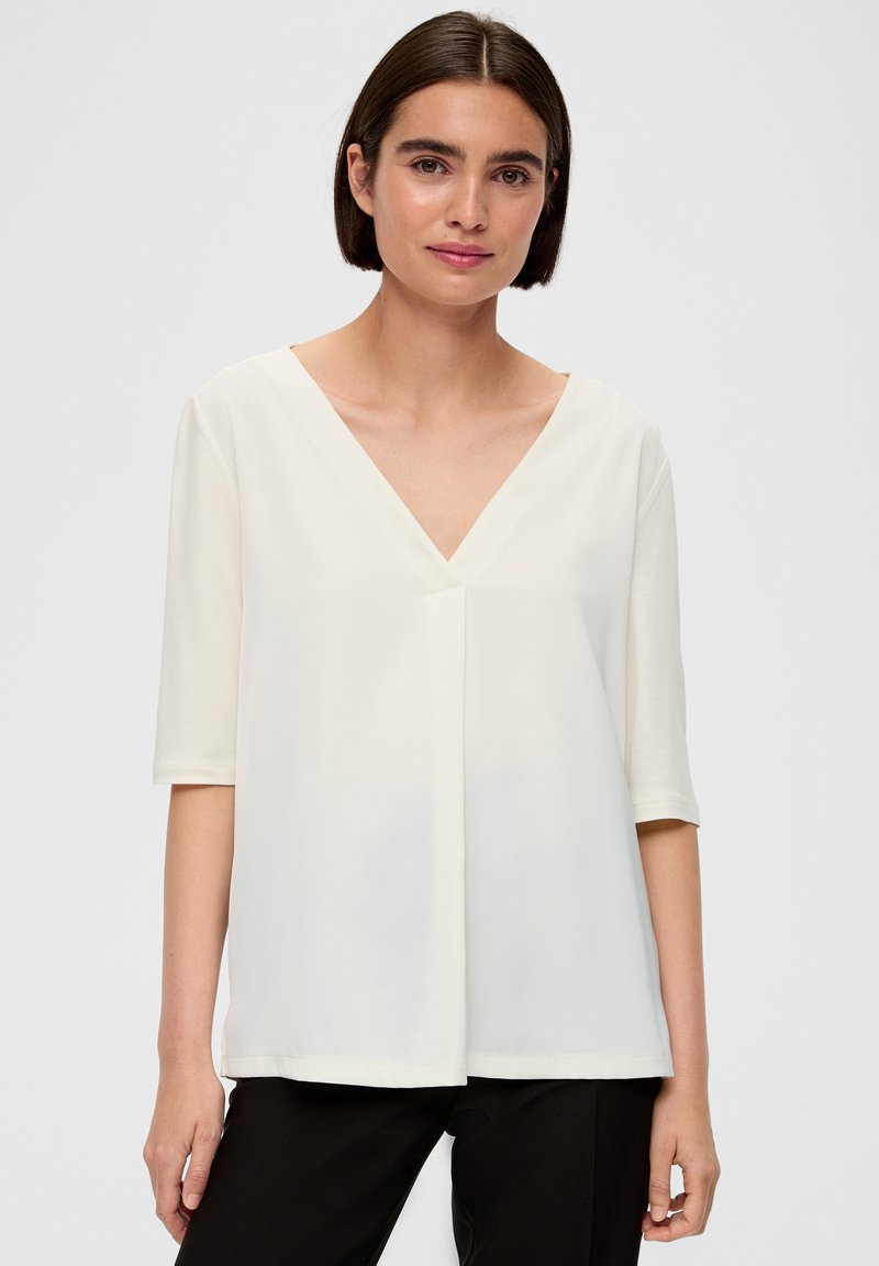 Biała bluzka z krótkim rękawem o dekolcie w kszta�łcie litery V, luźny krój i gładka tekstura; posiada delikatne plisowanie na środku i prosty dół.