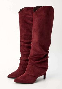 Bottes en suède bordeaux mi-hautes avec un design plissé, bout pointu et talon aiguille fin, présentant une texture lisse et un bord supérieur replié.