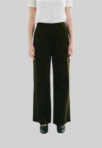 Pantalons en velours côtelé à jambes larges de couleur vert foncé, présentant une taille haute et un tissu texturé. Associés à des chaussures noires, le tout sur un fond gris.