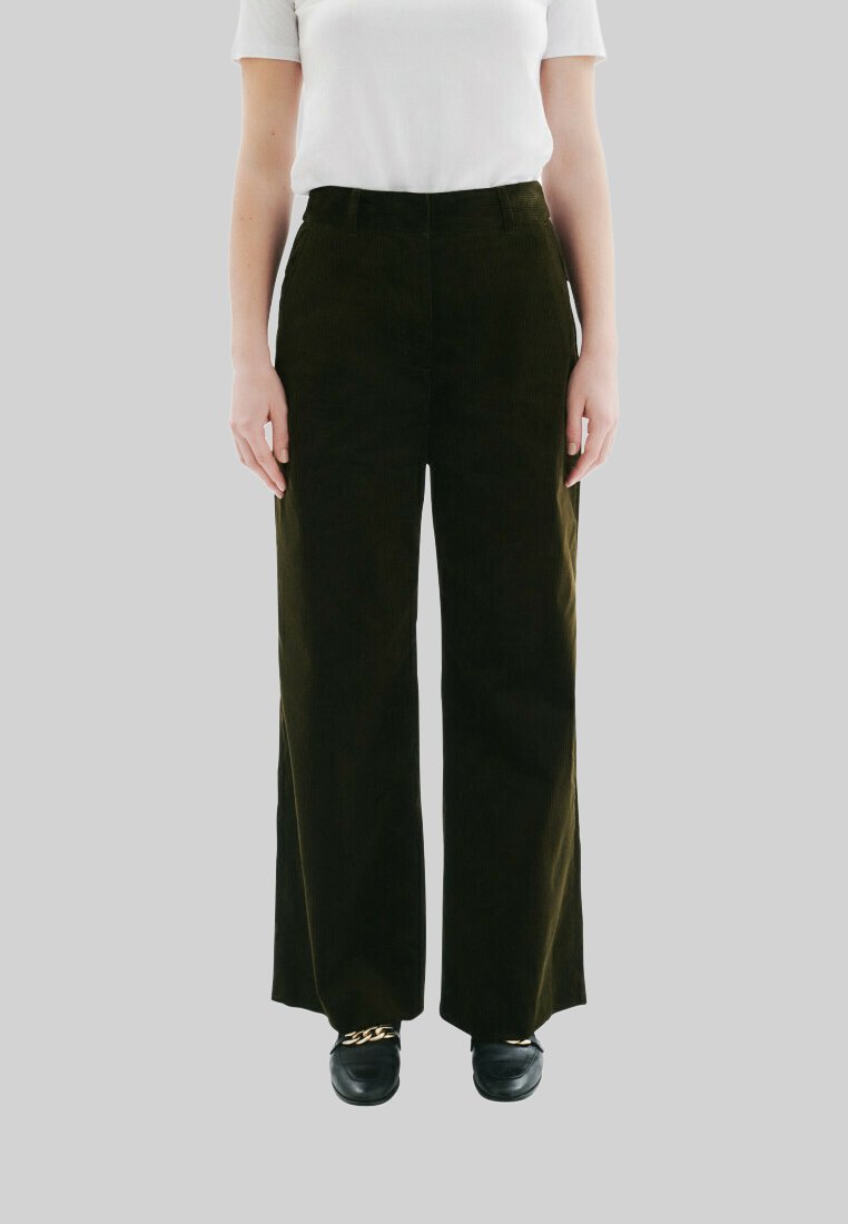 Pantalons en velours côtelé à jambes larges de couleur vert foncé, présentant une taille haute et un tissu texturé. Associés à des chaussures noires, le tout sur un fond gris.