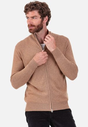 Pull à fermeture éclair couleur beige en tissu tricoté doux, doté d'un col et de poignets côtelés, avec une fermeture éclair à l'avant et une coupe décontractée.