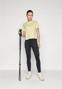 Light yellow short-sleeve shirt, black trouser leggings with pockets, holding a black trekking pole, wearing beige sneakers. Simple design.