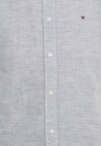 Ljusblå skjorta med knappar i en texturerad tyg med tunna vita ränder. Har vita knappar och en liten logotyp på vänster bröst.