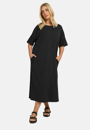 Robe noire, longueur genoux, en tissu doux, avec des manches courtes, des poches latérales et une coupe décontractée. Présente une silhouette droite et un design minimal.