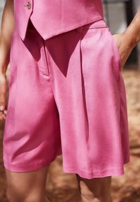 Shorts roses, ajustés, fabriqués en tissu lisse, avec poches avant et design plissé, offrant une coupe décontractée et un ourlet propre.