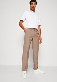 Bēša krāsas šūti taisnas bikses ar kabatām un gludu faktūru. Kombinētas ar baltu īsā piedurkņu T-kreklu un baltiem sporta apaviem.