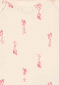 Lys beige stoff har et gjentatt mønster av rosa ballet-sko med sløyfer, myk tekstur, og design med rund hals som er egnet for spedbarn.