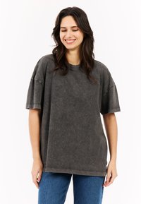 Overmaat grijze katoenen t-shirt met een gewassen textuur, korte mouwen, ronde halslijn en subtiele stikdetails, gecombineerd met blauwe jeans.