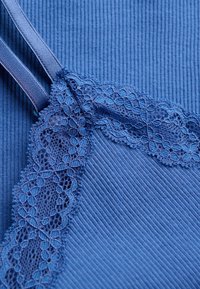 Blauer gerippter Stoff mit floralem Spitzenbesatz und verstellbarem Träger, zeigt detaillierte Textur und Nähte.