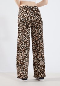 Pantalon à jambes larges à imprimé léopard en tissu doux, doté d'une taille haute, de poches arrière et d'une coupe ample. Coutures renforcées et texture lisse.