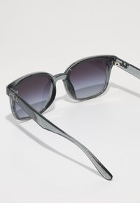 Ochelari de soare din plastic gri, cu lentile degrade, formă rotundă și design elegant al bratelor. Logo-ul imprimat pe lentila stângă.