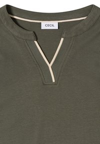 Encolure de chemise vert olive avec une coupe en V, une bordure beige et une étiquette en tissu portant la mention "CECIL" au niveau du col arrière.