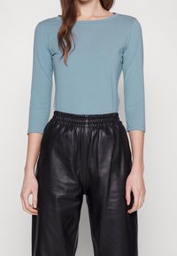 Långärmad, ljusblå topp i mjukt tyg, kombinerad med högmidjade svarta läderbyxor med elastisk midja och slät textur.