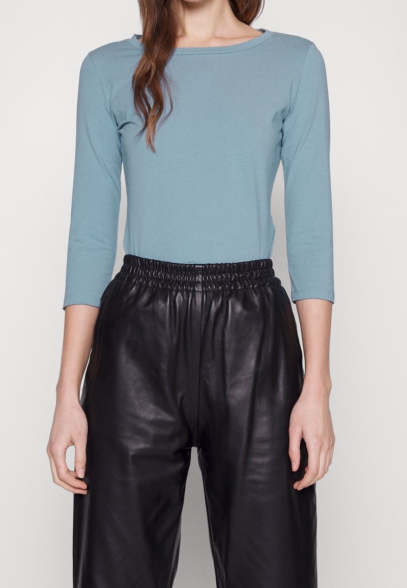 Långärmad, ljusblå topp i mjukt tyg, kombinerad med högmidjade svarta läderbyxor med elastisk midja och slät textur.