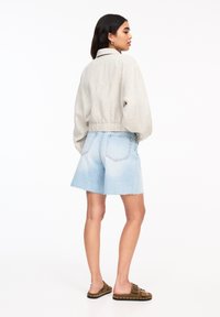 Lichtgrijze cropped jas met een kraag, gecombineerd met blauwe denim shorts met een rafelige zoom. Draag het met bruine instapsandalen.
