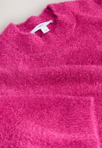 Purpurinis rožinis megztinis su minkšta tekstūra, apvalia apykakle ir priekinėje dalyje esančia kišene. Etiketėje parašyta „NEXT“. Dizainas yra vientisos spalvos be raštų.