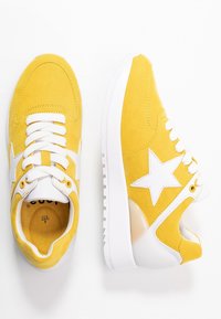 Baskets en daim jaune avec des accents blancs, présentant un design étoile, une surface texturée, un laçage à l'avant et une semelle blanche épaisse.