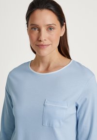 Lichtblauw langemouw shirt van zachte stof, met een ronde halslijn en een kleine borstzak met zichtbare stikdetails.