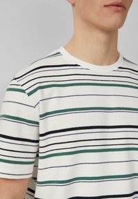 Gestreepte t-shirt met korte mouwen in het wit met groene, zwarte en paarse horizontale lijnen. Gemaakt van katoen met een zachte textuur en een ronde hals.
