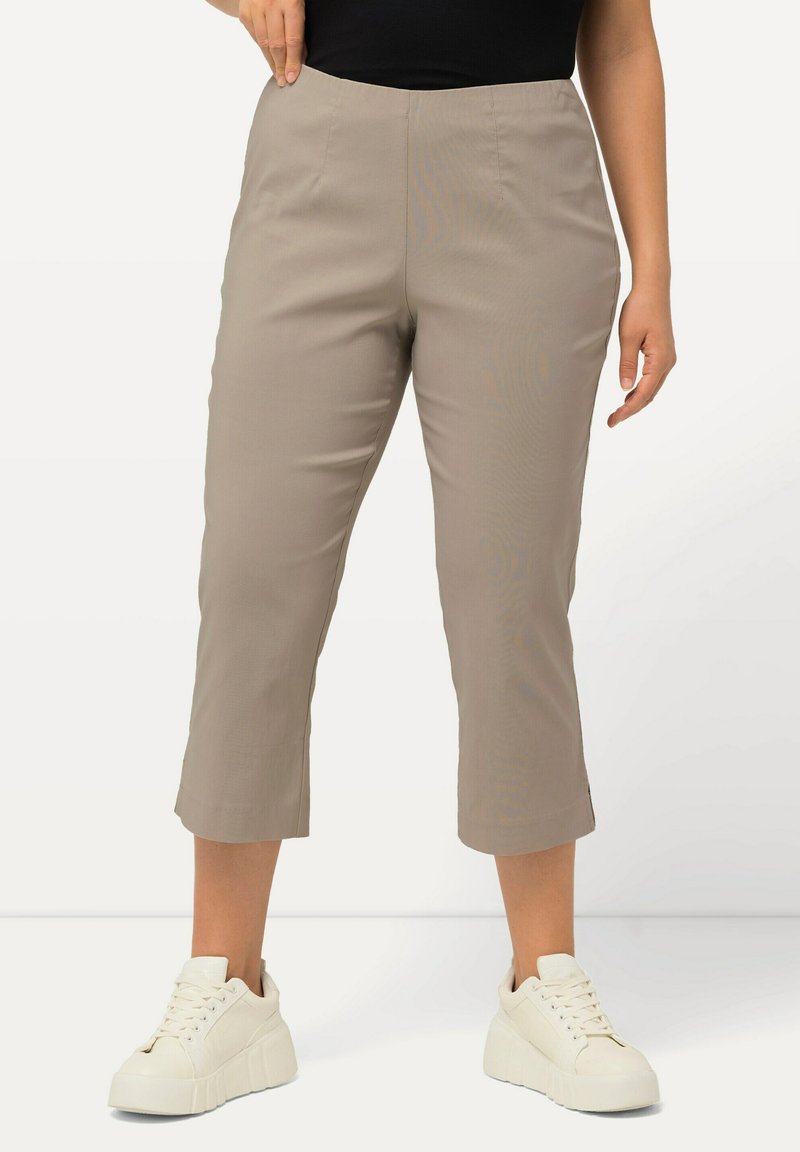 Pantaloni beige a vita alta, con una texture liscia, caratterizzati da cuciture laterali e un taglio dritto. Abbinati a sneakers bianche.