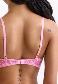 Roze kanten bh met verstelbare satijnen bandjes en gouden hardware. Het verfijnde bloemenpatroon siert de band, met een haak- en oogsluiting.
