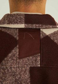 Bruin-gepatroneerde fleece jas met een gestructureerd oppervlak, voorzien van een effen bruine accentpatch en zichtbare stiksels bij de kraag.