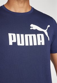 Camiseta de algodón azul marino con cuello redondo, que presenta un gran logo blanco de "PUMA" y un gráfico de un puma saltando en el hombro izquierdo.