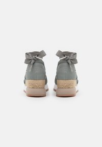 Zapatillas gris de altura de tobillo con parte superior de tela, suela intermedia trenzada estilo espadrille y cintas decorativas en la parte trasera. Suela de goma.