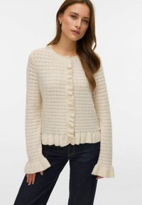 Krämfärgad stickad cardigan med ett strukturerat mönster, rund halsringning, volangprydd knappslå och utsvängda ärmar.