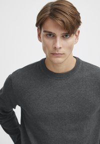 Suéter gris de cuello redondo hecho de una tela suave, con puños y cuello acanalados, de textura suave y diseño simple.
