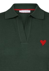 Dunkelgrünes Poloshirt mit klassischem Kragen, gerippter Textur und einem roten Herz, das auf der linken Seite gestickt ist. Markenetikett sichtbar.