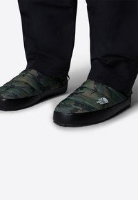 Pantofole verdi con motivo mimetico, design trapuntato, suola in gomma nera e marchio sul lato. Si adattano perfettamente ai piedi.