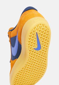 Baskets orange et marine avec un logo Nike en bleu sur le côté et la semelle, semelle jaune texturée avec un motif de bande de roulement.