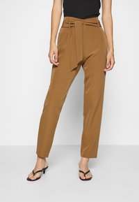 Pantalones marrones de cintura alta con detalle de cinturón atado y piernas rectas. Tela suave y diseño ajustado. Combinados con sandalias negras.